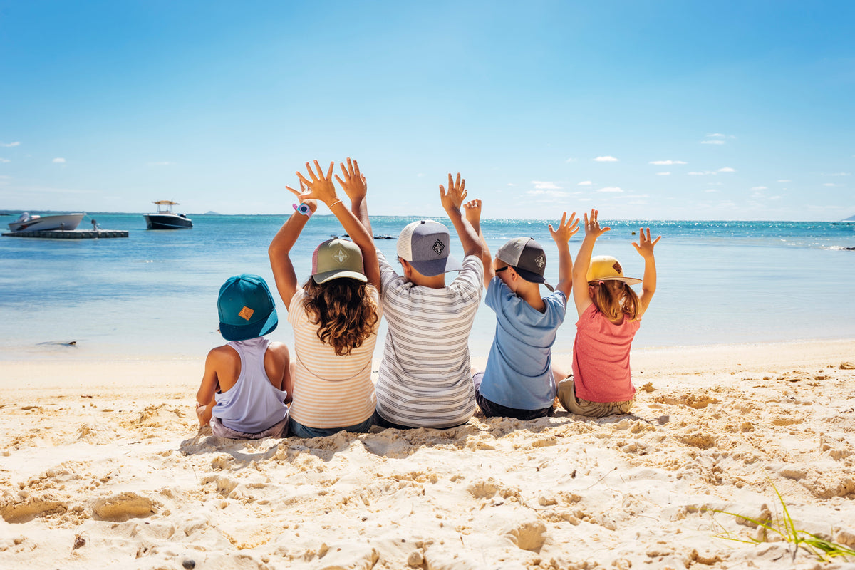 Kinder sitzen am Strand und tragen alle Caps