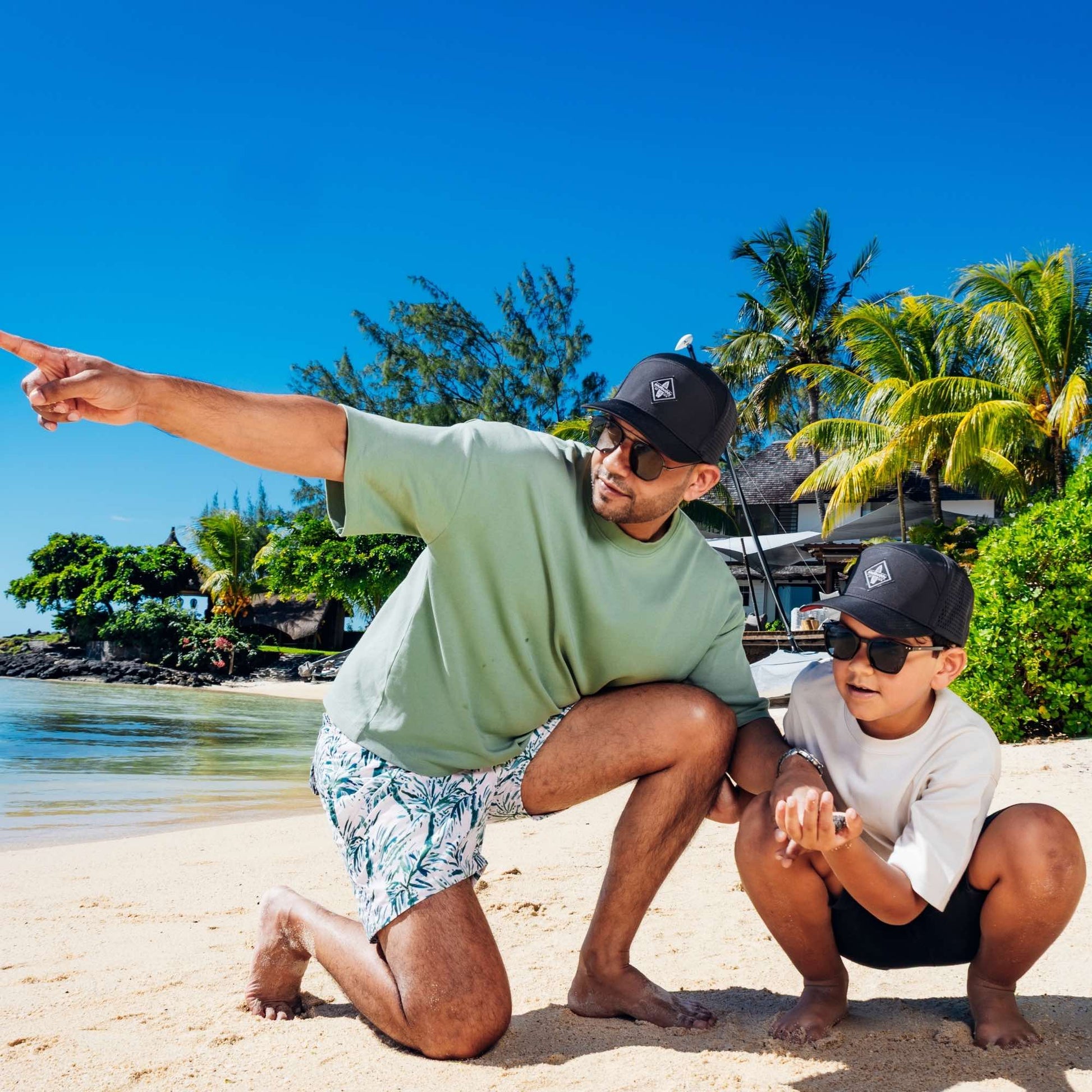Vater und Sohn mit schwarzen Snapback Caps im Partnerlook entdecken gemeinsam den Strand bei sonnigem Sommerwetter