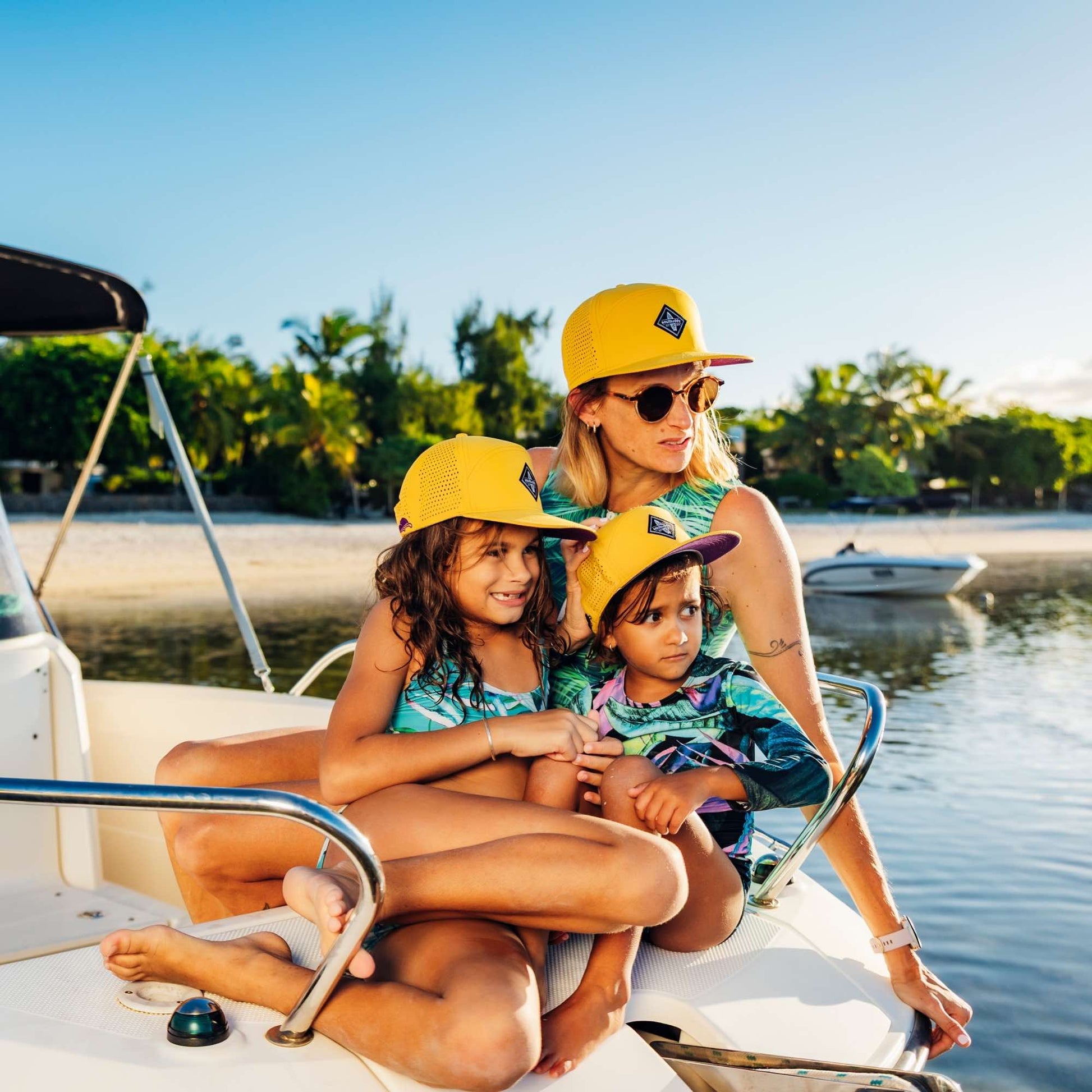 Mutter und zwei Kinder tragen gelbe Snapback Caps im Partnerlook und genießen gemeinsamen Bootsausflug am Meer bei sommerlichem Wetter