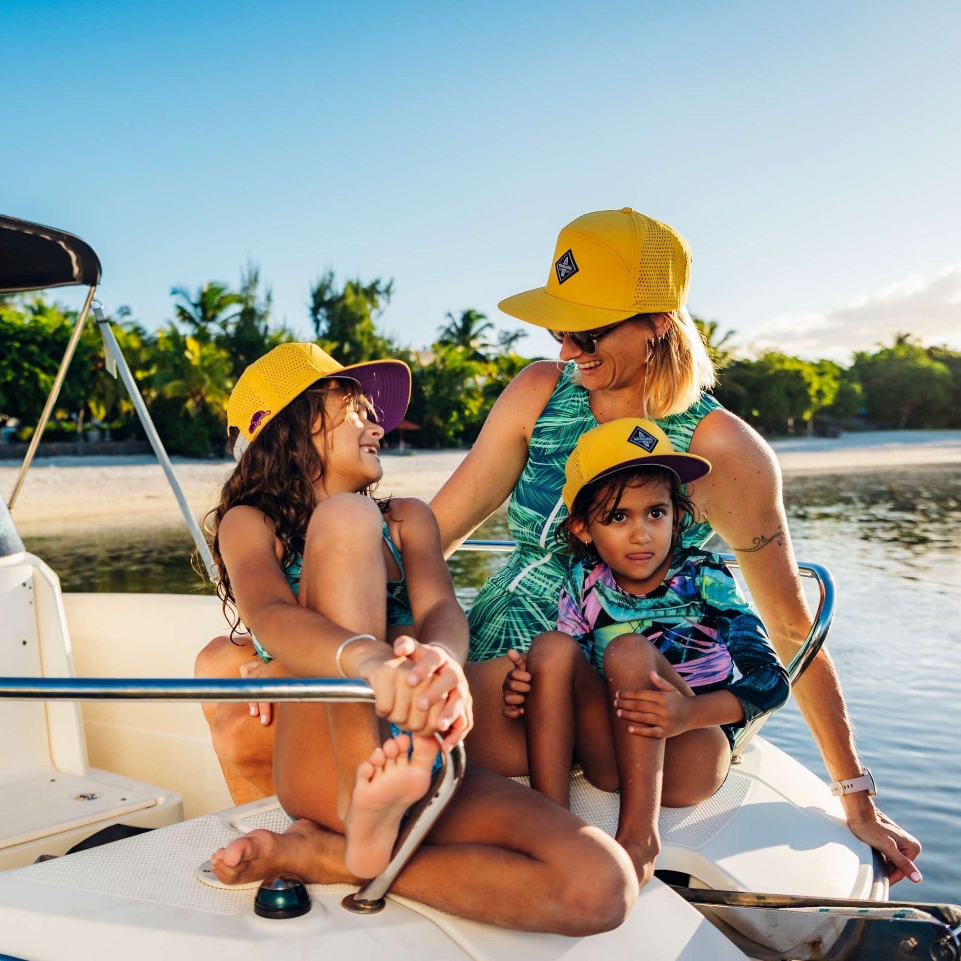 Mutter und zwei Kinder mit gelben Snapback Caps im Partnerlook genießen gemeinsamen Bootsausflug am Strand bei sommerlichem Wetter