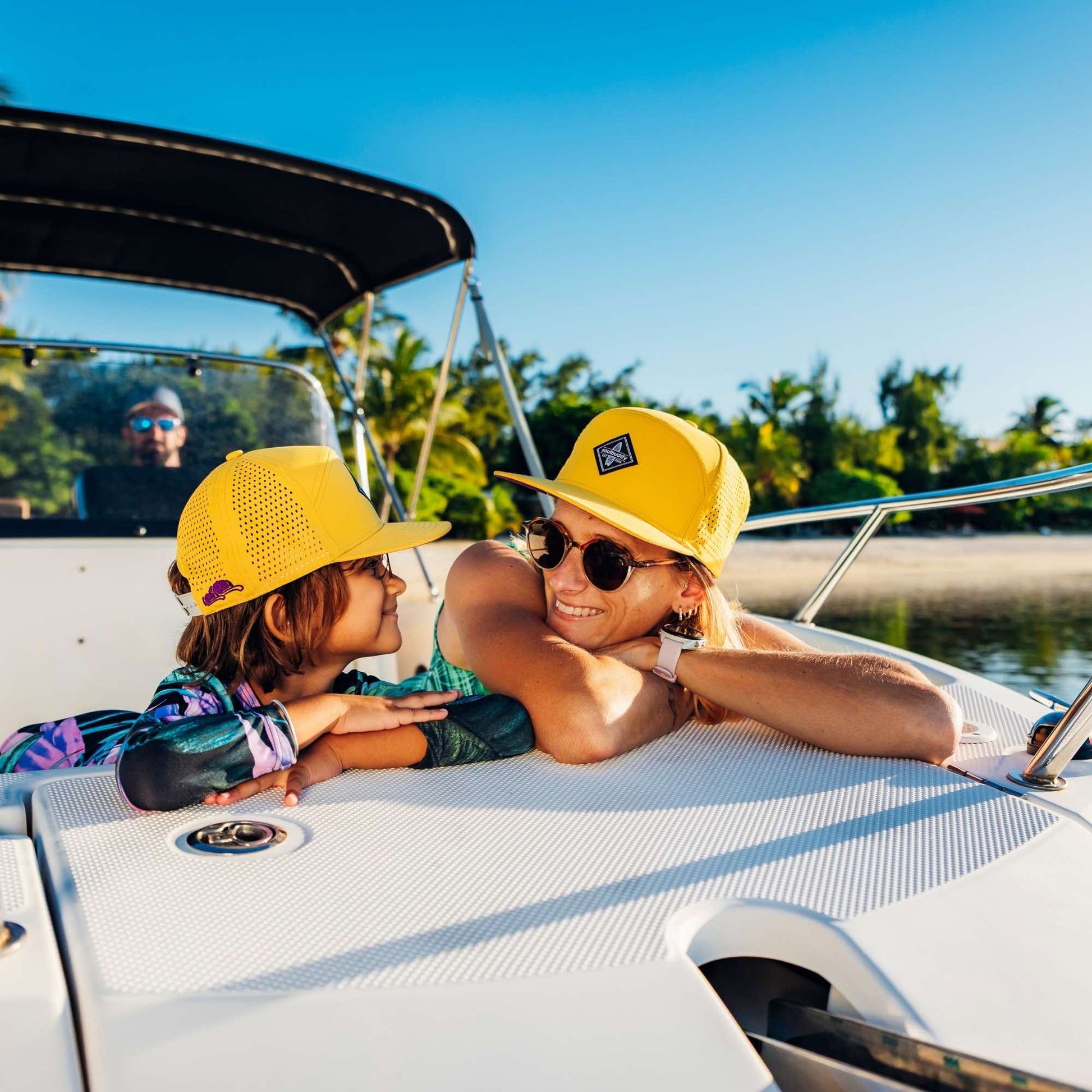Mutter und zwei Kinder mit gelben Snapback Caps im Partnerlook genießen gemeinsamen Bootsausflug am Strand bei sommerlichem Wetter
