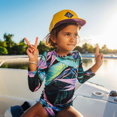 Soulbuddy Kinder Performance Cap – Kind mit gelber Cap auf einem Boot bei Sonnenuntergang