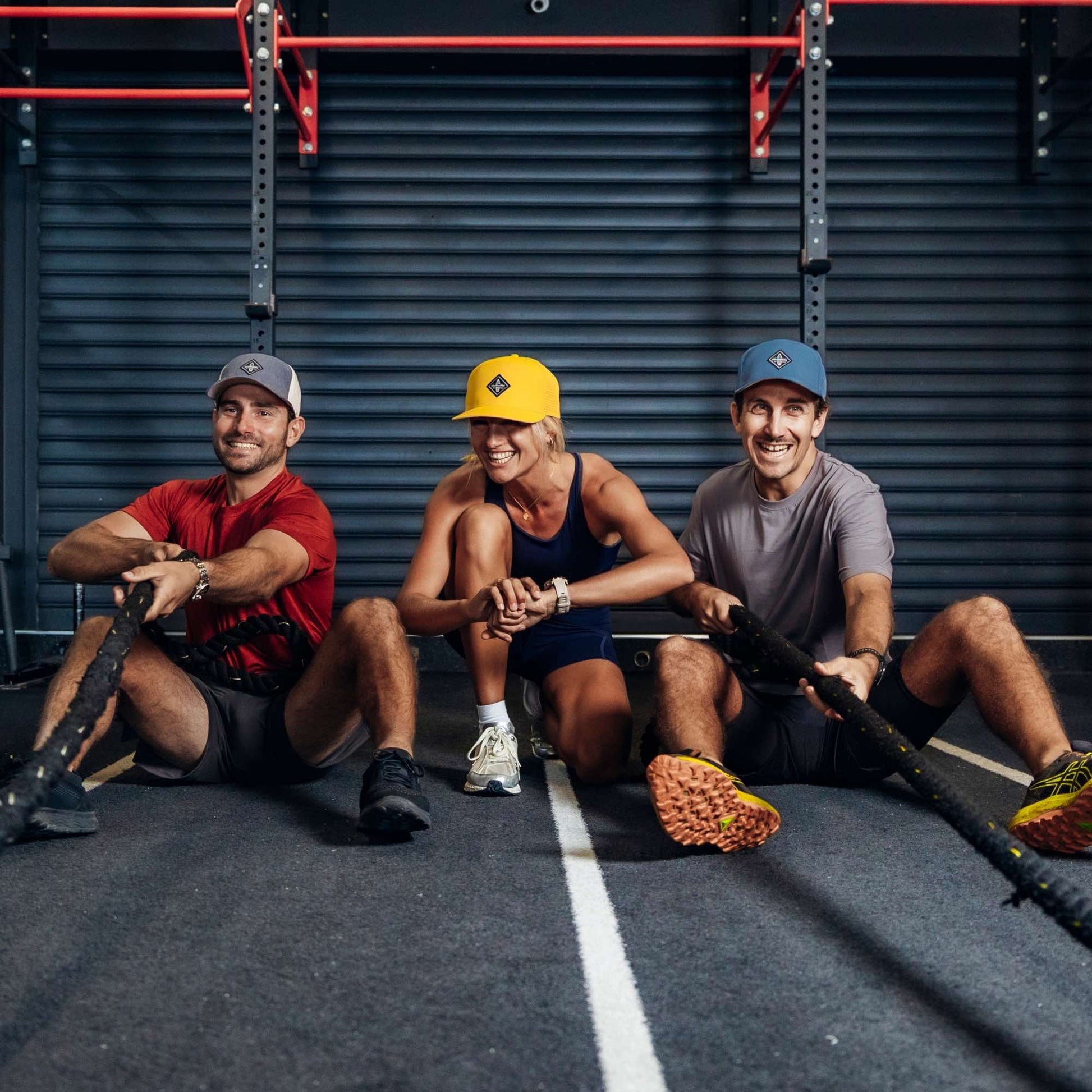 Drei sportliche Personen tragen Performance Snapback Caps beim gemeinsamen Training mit Battle Ropes im Fitnessstudio