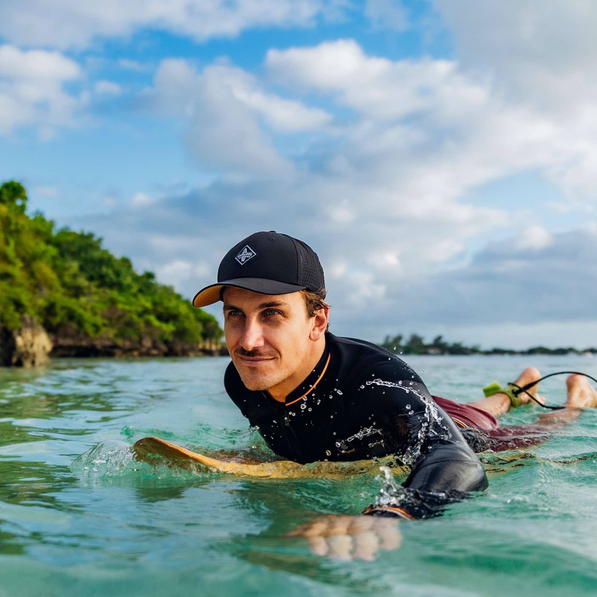 Sportlicher Mann trägt schwarze Snapback Cap beim entspannten Surfen im Meer vor tropischer Küste bei sonnigem Wetter
