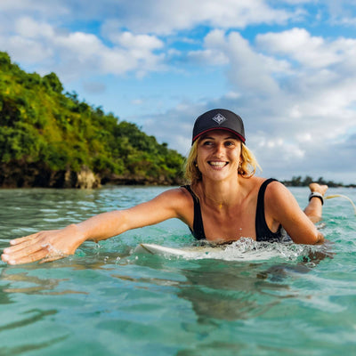 Soulbuddy Performance Cap für Damen und Herren – sportliche Frau mit schwarzer Cap beim Surfen vor tropischer Küste